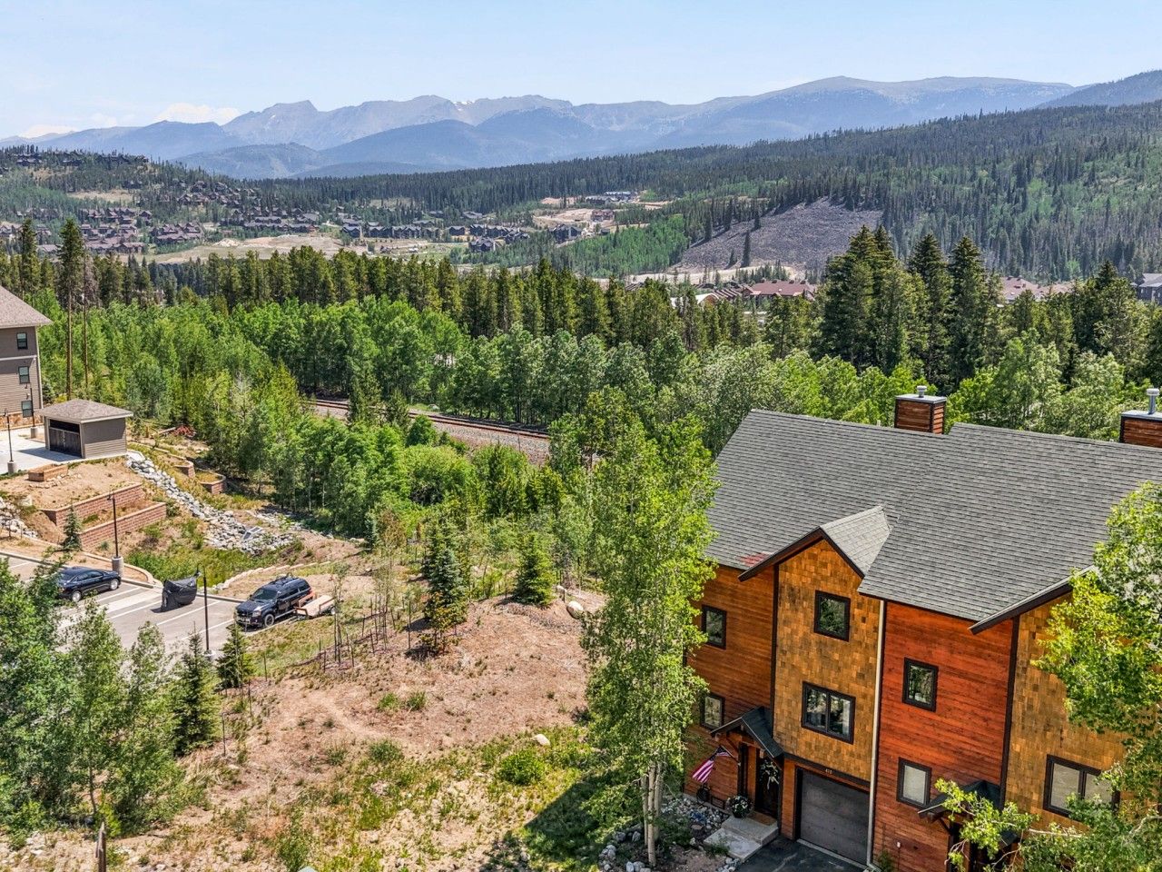 A residential area with a large wooden house, a paved driveway, and a clear view of a mountainous landscape.
