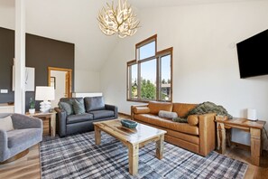 A modern living room with a grey sofa, a brown leather sofa, a wooden coffee table, and a large window providing a view of the outdoors.