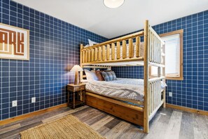 A bunk bed room with a wooden frame, a nightstand with a lamp, and a framed picture on the wall.