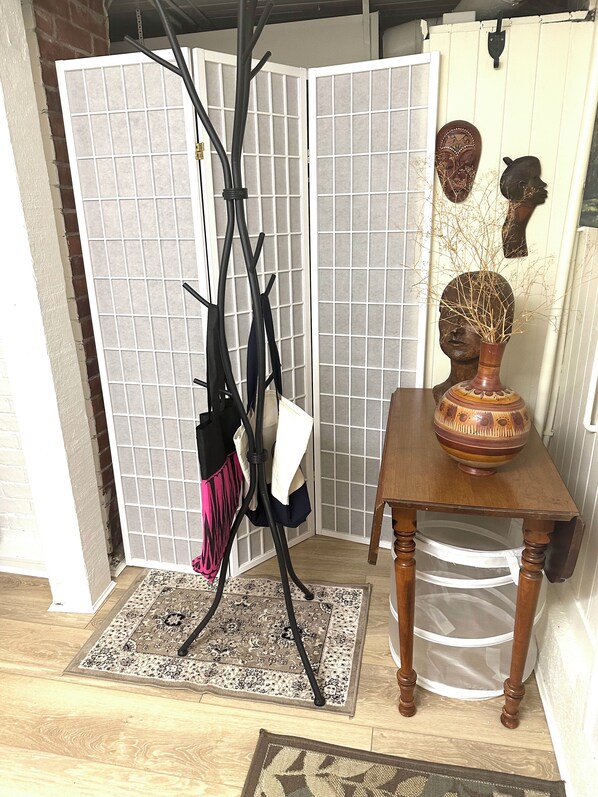 A room with a black floor lamp, a patterned rug, a wooden table with a vase, and decorative masks on the wall.