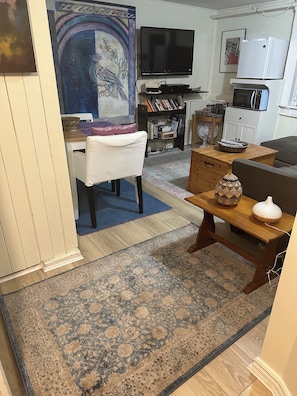 A living room with a television, bookshelves, a dining table with chairs, a patterned rug, and a decorative vase. - Private Artist's Suite & Garden | Commercial Drive (Vancouver)