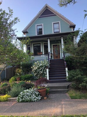 A two-story house with a front porch, a staircase, and a garden with various plants and flowers. - Private Artist's Suite & Garden | Commercial Drive (Vancouver)