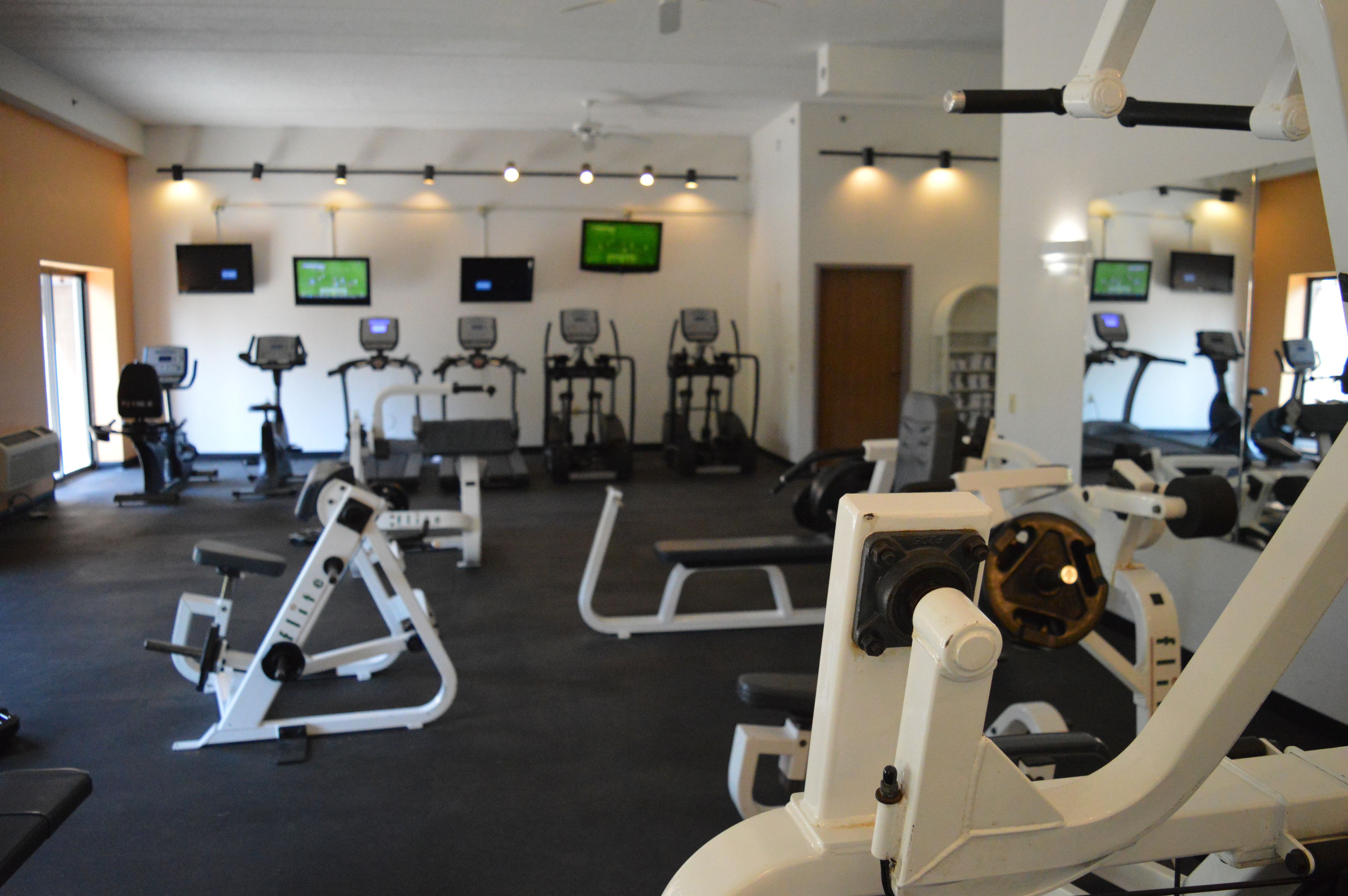 Ett gym med olika typer av träningsutrustning, inklusive löpband, motionscyklar och styrketräningsmaskiner.