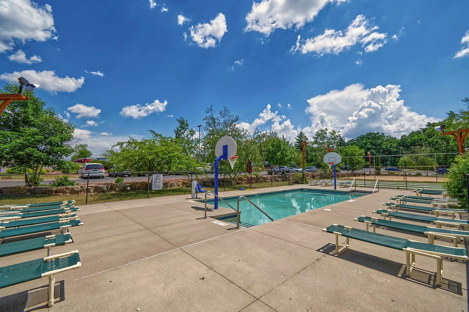 A pool area with multiple basketball hoops, green benches, and a clear blue sky.