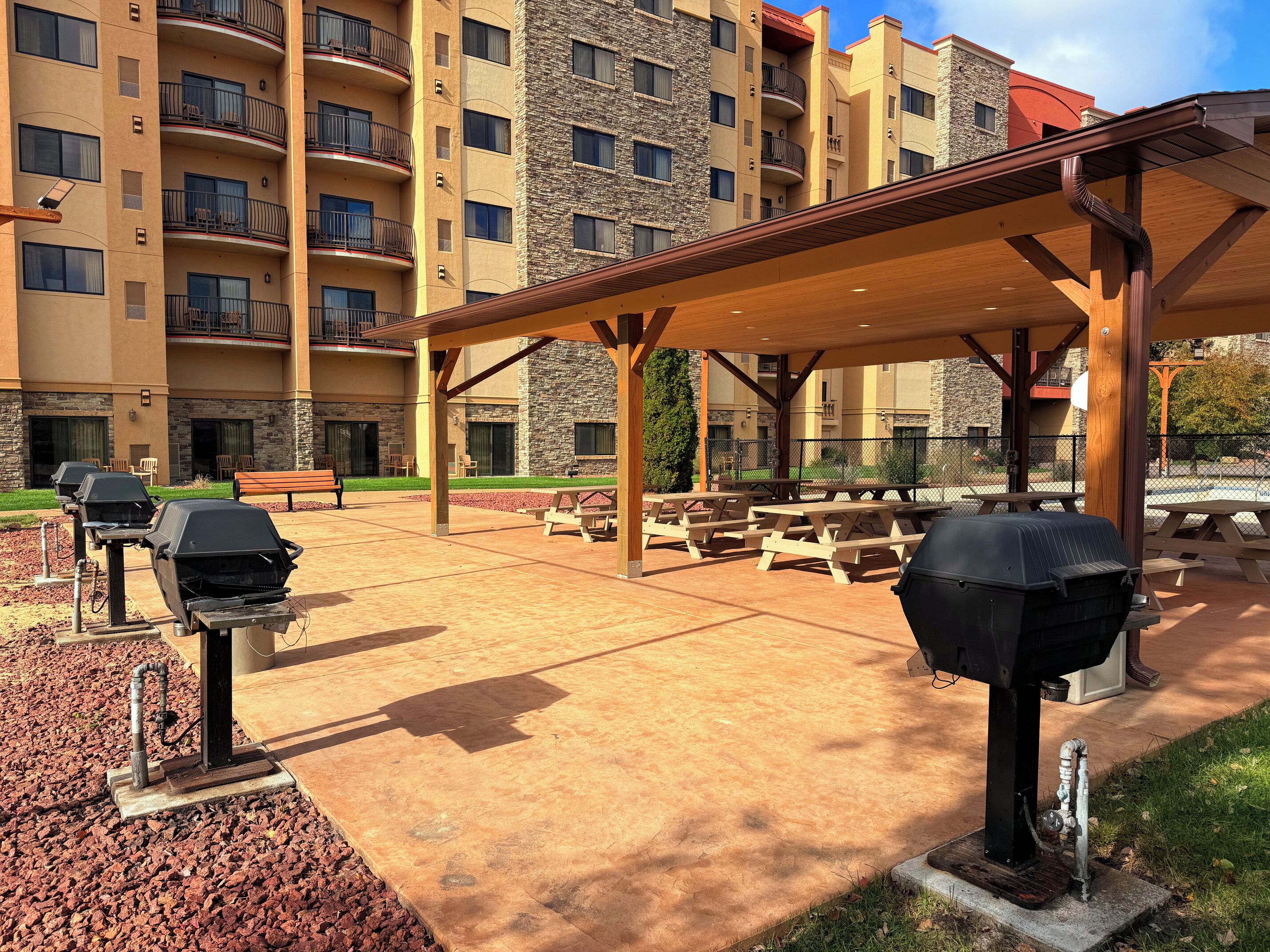 An outdoor patio area with barbecue grills, picnic tables, and a covered seating area.