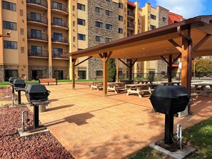 Un patio exterior con parrillas, mesas de picnic y un área de estar cubierta.