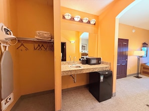 Un baño de hotel con lavamanos, espejo, toallero y un refrigerador pequeño.