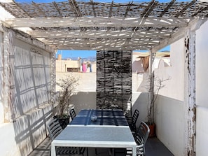 A covered outdoor dining area with a table and chairs, a pergola overhead, and a view of buildings in the background. - Holiday House in Nerja With Sea Views (Nerja)