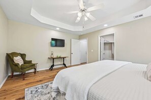 Une chambre à coucher comprenant un lit, un ventilateur de plafond, une télévision, une chaise et une table.
