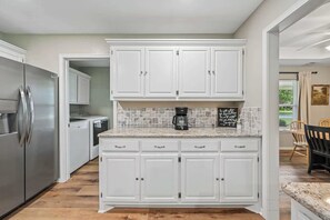 Eine Küche mit weißen Schränken, einem Edelstahl-Kühlschrank, einer Kaffeemaschine und einer gefliesten Spritzschutzwand.