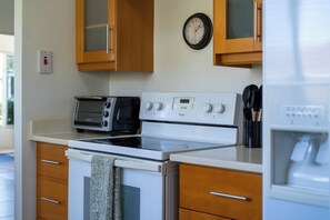 A kitchen with a white stove, a black toaster, wooden cabinets, and a wall clock. - Richmond Retreat Gated Pool Beach Access (St. Ann's Bay)