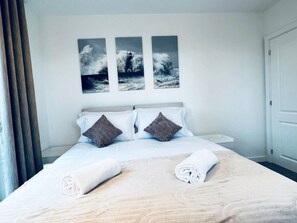 Ett hotellrum med en säng, kuddar, ett nattduksbord och tre fotografier som hänger på väggen.