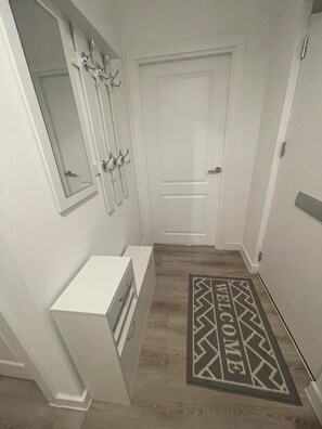 A hallway with a white door, a coat rack, a small white cabinet, and a welcome mat. - 2BR Apt Near Birmingham City Centre | Sleeps 6 (Birmingham)