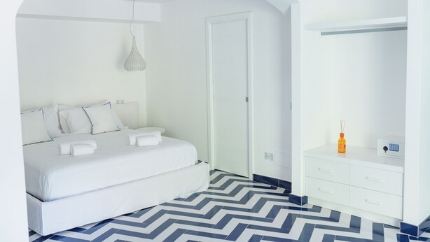 A modern hotel room with a bed, a white dresser, and a mirror. - Vrbo Property (Campania)