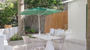 An outdoor patio with a table and chairs, a green umbrella, and a stone wall in the background. - Vrbo Property (Campania)
