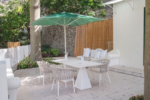 An outdoor patio with a table and chairs, a green umbrella, and a stone wall in the background. - Vrbo Property (Campania)