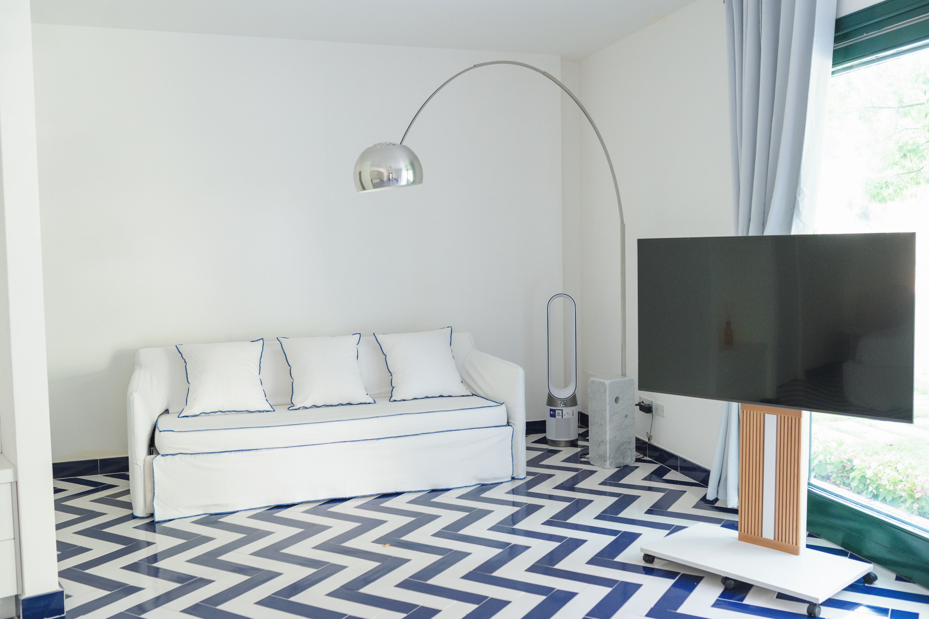 Een moderne woonkamer met een bank, een staande lamp, een flatscreen televisie en een vloer met een patroon.