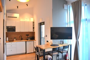 A compact kitchen with white cabinets, a built-in microwave, and a flat-screen TV on a wooden table.