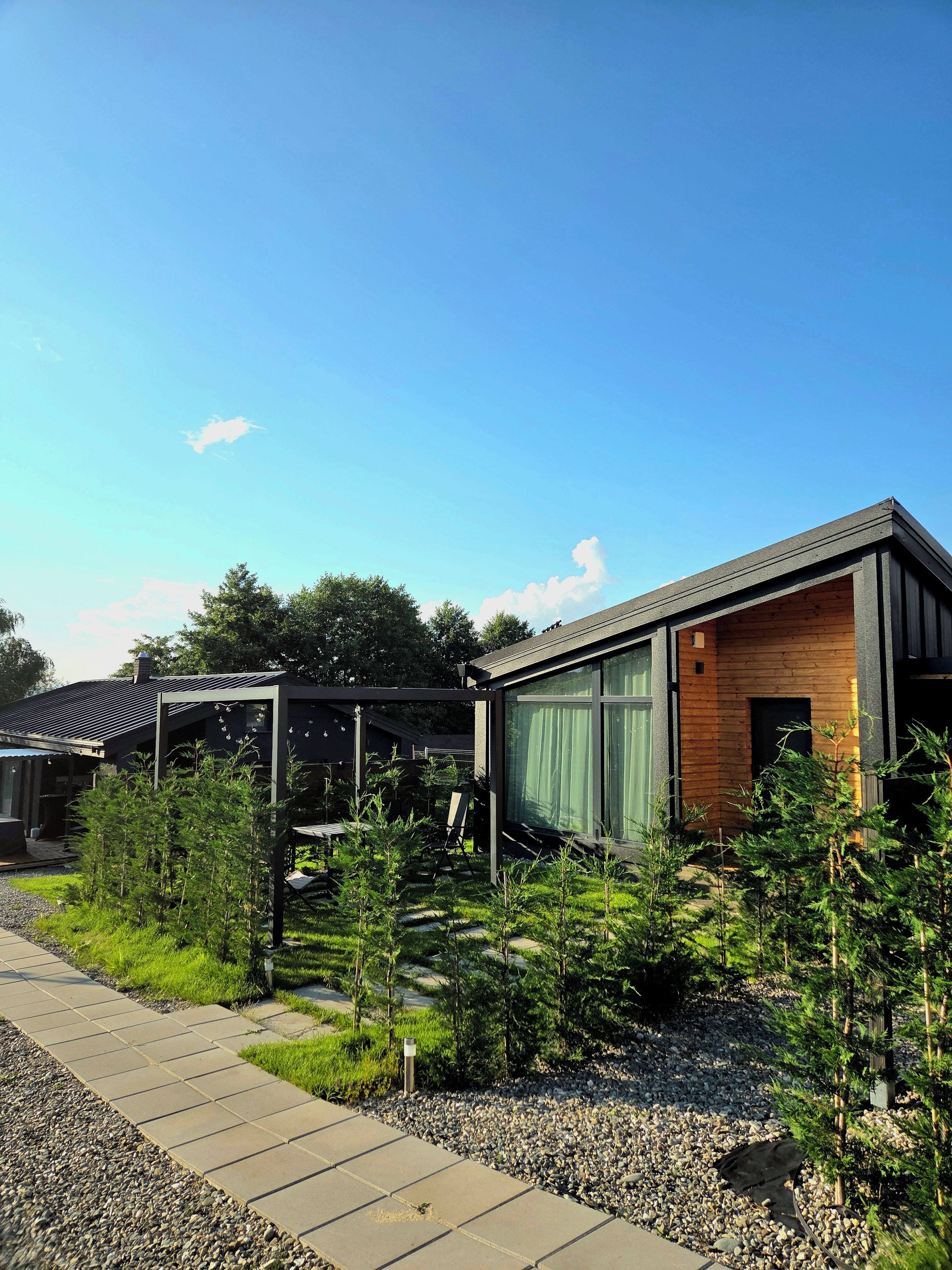 A modern building with a wooden exterior and large windows, surrounded by a well-maintained garden with young trees and a gravel pathway.