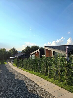 A modern building with a covered outdoor area, a gravel pathway, and a row of small trees.