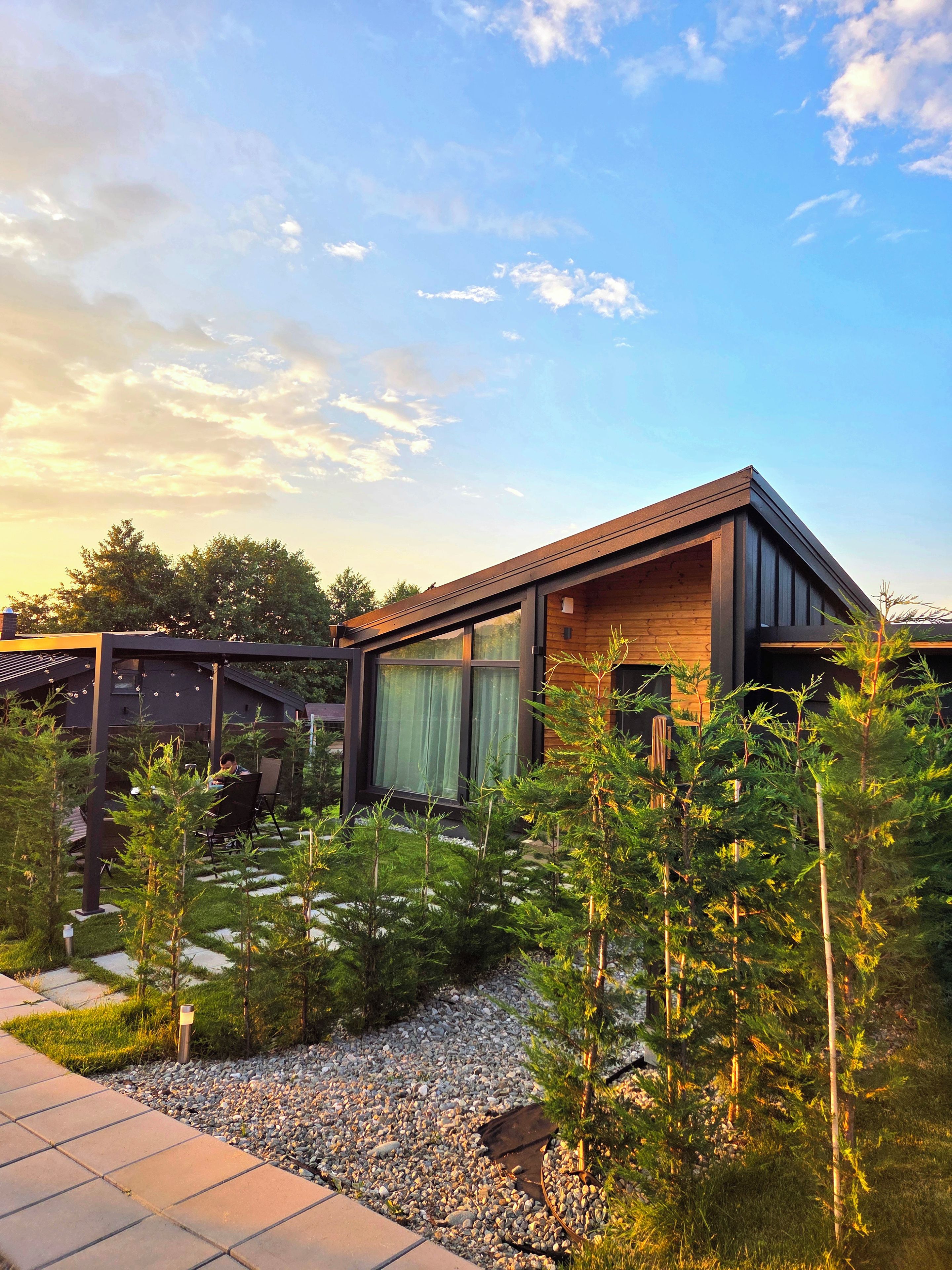 Une maison moderne avec une façade en bois, un espace extérieur couvert et un jardin planté de jeunes arbres.