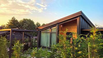 Une maison moderne avec une façade en bois, un espace extérieur couvert et un jardin planté de jeunes arbres.