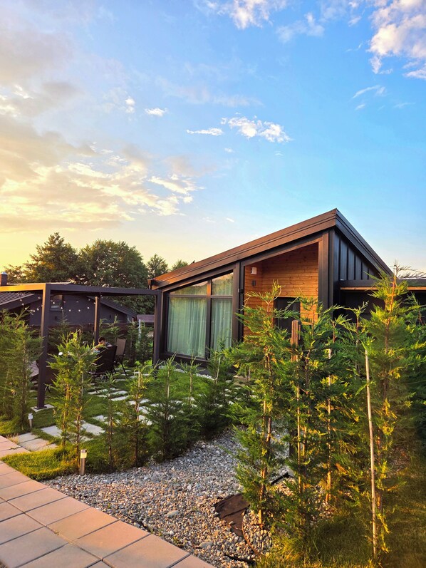 A modern house with a wooden exterior, a covered outdoor area, and a garden with young trees.