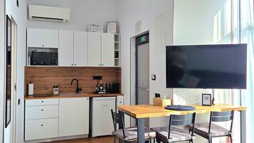 Une cuisine moderne avec des meubles blancs, un four à micro-ondes et un évier. On y trouve également un coin repas avec une table et des chaises, ainsi qu’un grand téléviseur à écran plat fixé au mur.
