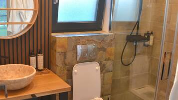 Une salle de bain moderne avec un mur en pierre, un grand miroir, un lavabo, des toilettes et une douche séparée par une paroi de verre.