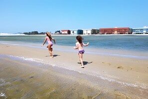 Two children playing on a sandy beach with buildings in the background. - Apartamento Pôr do Sol (Arraial do Cabo)