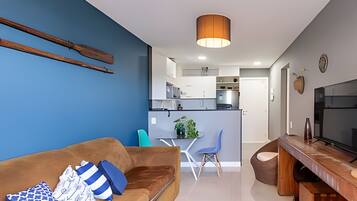 Una sala moderna con un sofá, un comedor con sillas, una cocina al fondo y un televisor sobre un mueble de madera.