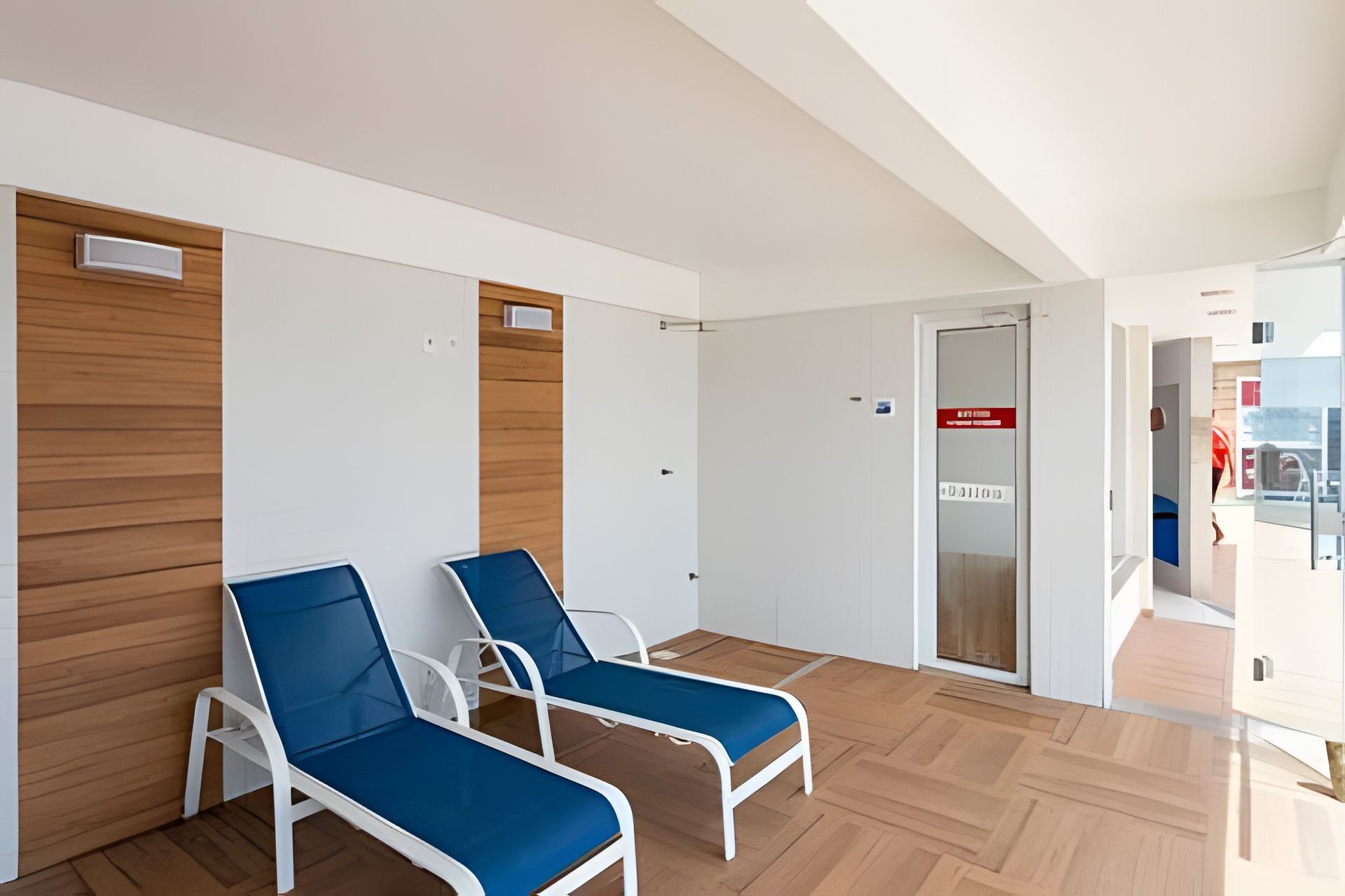 A waiting area with two blue lounge chairs, wooden panel walls, and a glass door leading outside.