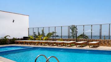 Piscina com espreguiçadeiras e vista para o oceano.