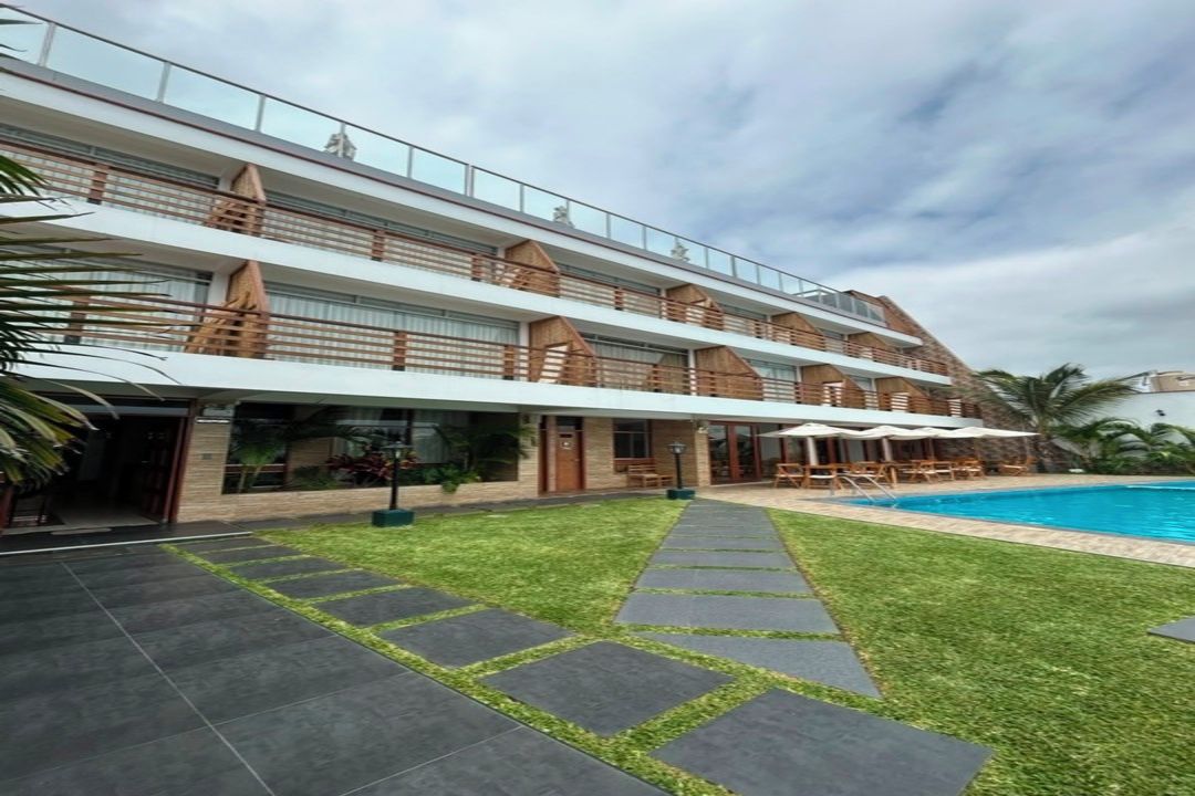 Um hotel com vários andares, piscina, área de estar externa e gramado bem cuidado.