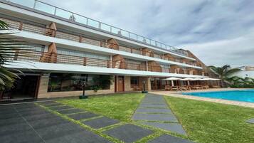 Um hotel com vários andares, piscina, área de estar externa e gramado bem cuidado.