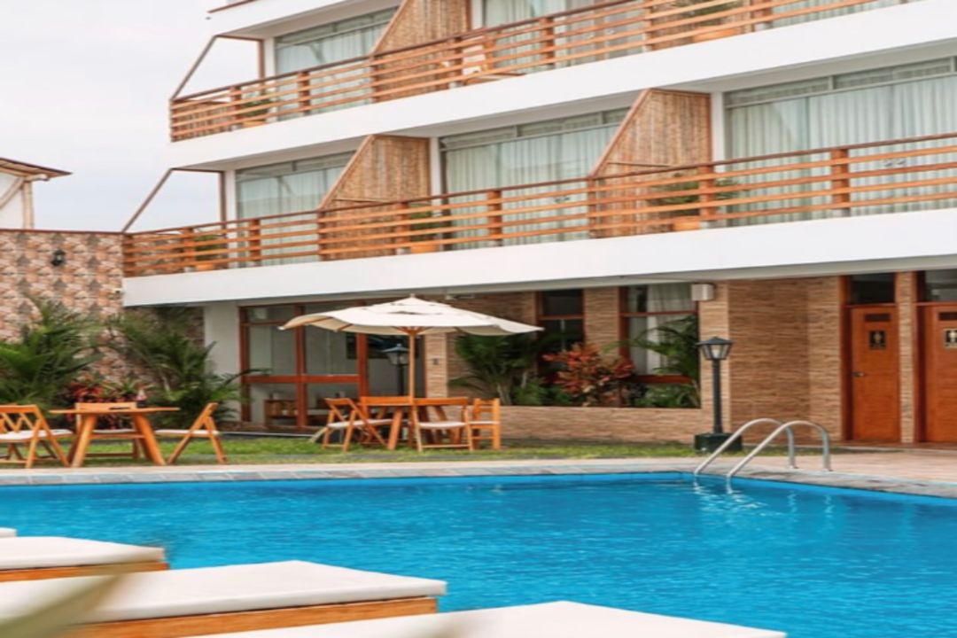 A modern hotel with a swimming pool, outdoor seating, and a multi-story building with balconies.