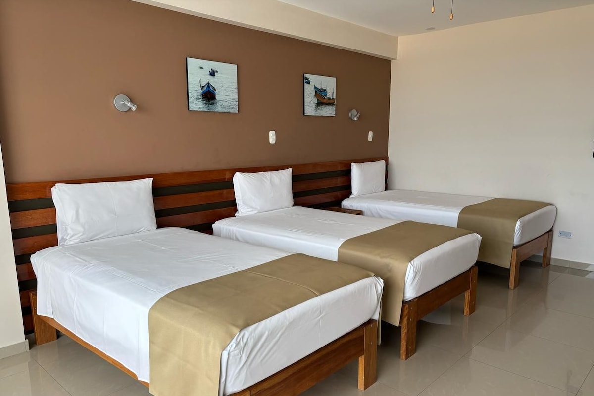 A hotel room with three single beds, a wooden headboard, white bedding, and two wall-mounted light fixtures.