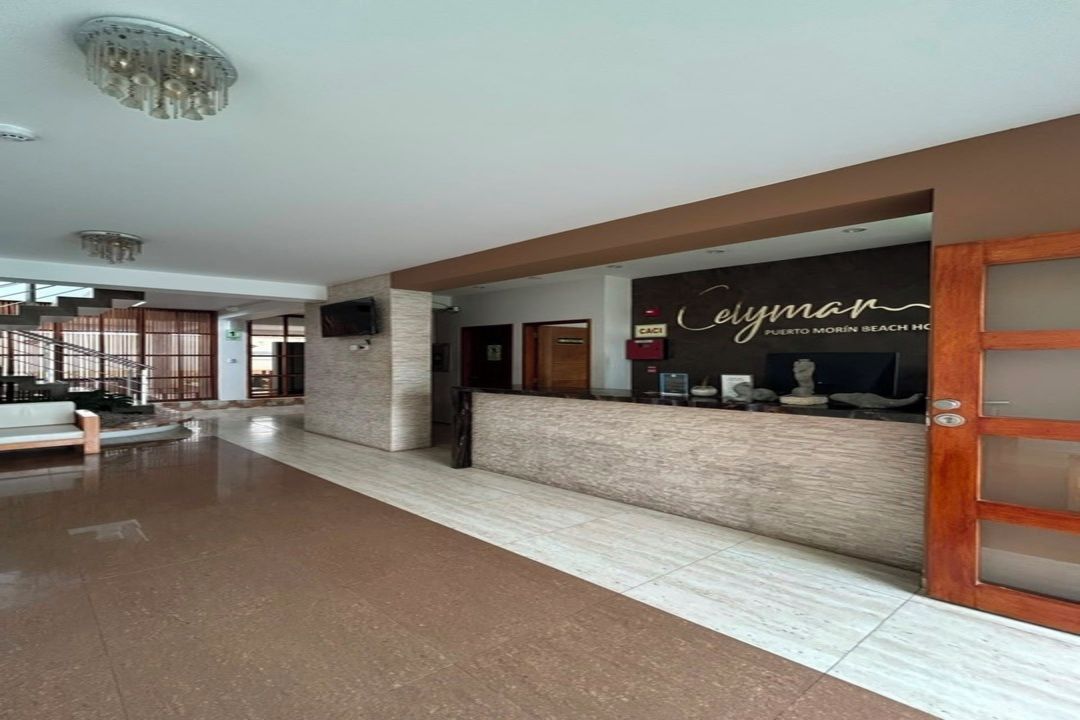 Área de recepção de hotel com balcão, escada e vista para o exterior.