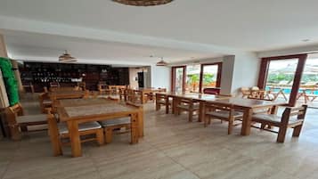Ein großzügiger Innenbereich mit mehreren Holztischen und -stühlen, einer Bar mit Flaschenregalen und großen Fenstern mit Blick ins Freie.