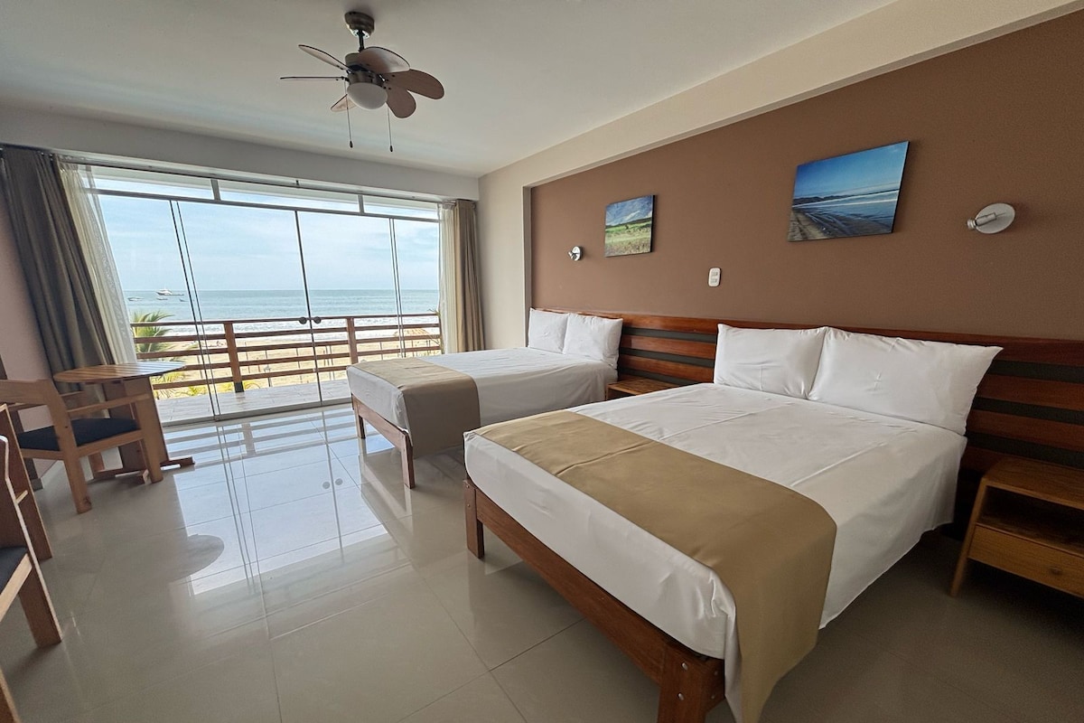 A hotel room with two beds, a ceiling fan, a view of the beach, and a wooden chair.