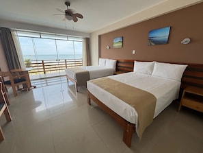 A hotel room with two beds, a ceiling fan, a view of the beach, and a wooden chair. - CELYMAR HOTEL (Viru)
