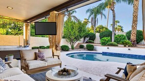 Zona junto a la piscina con sofá, televisor de pantalla plana y piscina.