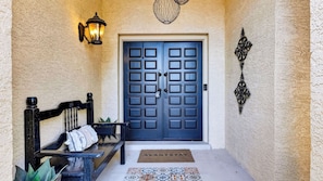 A dark blue door with a white doormat in front, a bench with a cushion, and a wall-mounted light fixture. - Casa Talavera by Avantstay Pool + Hot Tub + Fire Pit + BBQ Mins to Golf (Scottsdale)