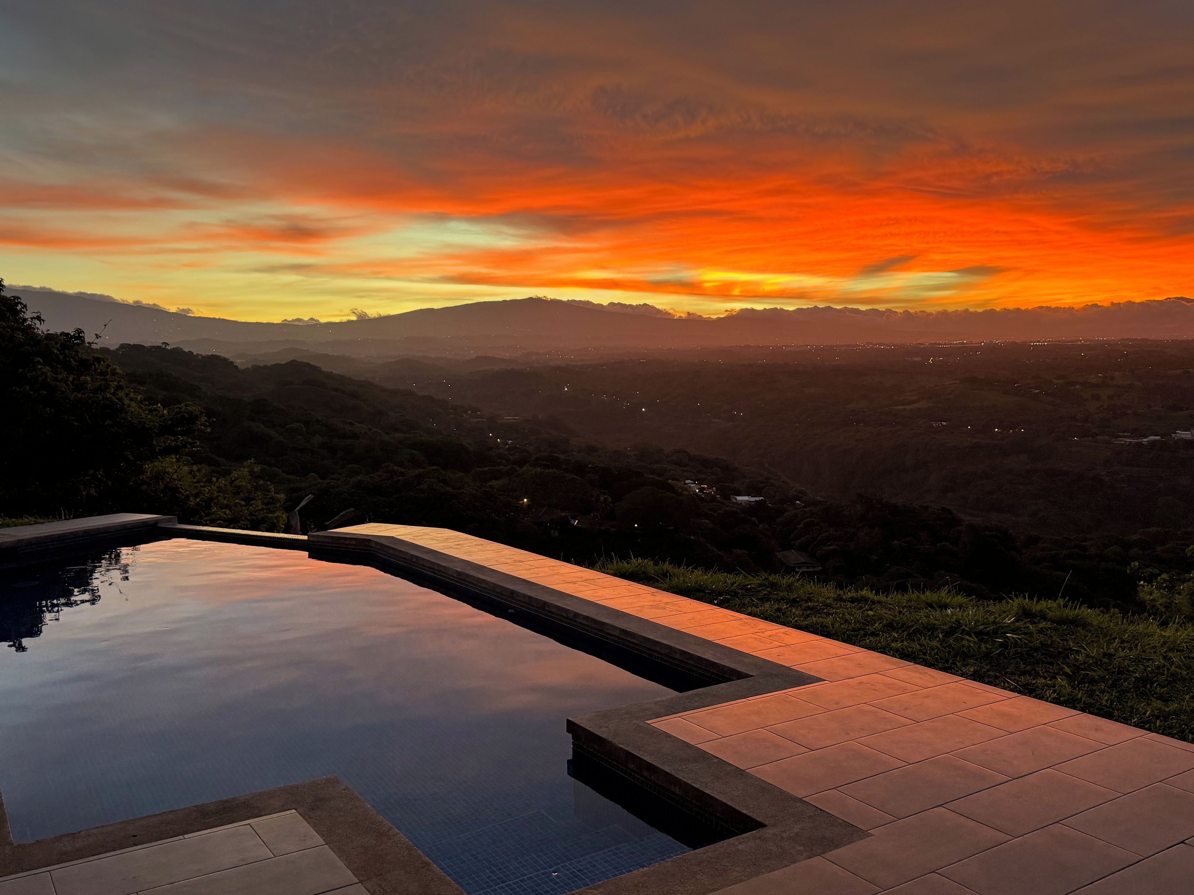 A swimming pool with a view of a sunset over a mountainous landscape.