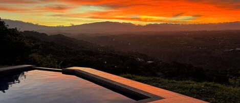 A swimming pool with a view of a sunset over a mountainous landscape.