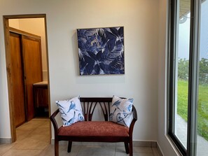 A room with a wooden bench, a wall-mounted abstract painting, and a window with a view of greenery. - Villa Aleva: Private Pool, Panoramic Views & 30+ Night Stays (Atenas)