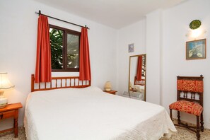 A bedroom with a bed, a window with curtains, a bedside lamp, a mirror, a small table with a lamp, and a chair. - Studio in Nerja Near Carabeillo Beach (Nerja)