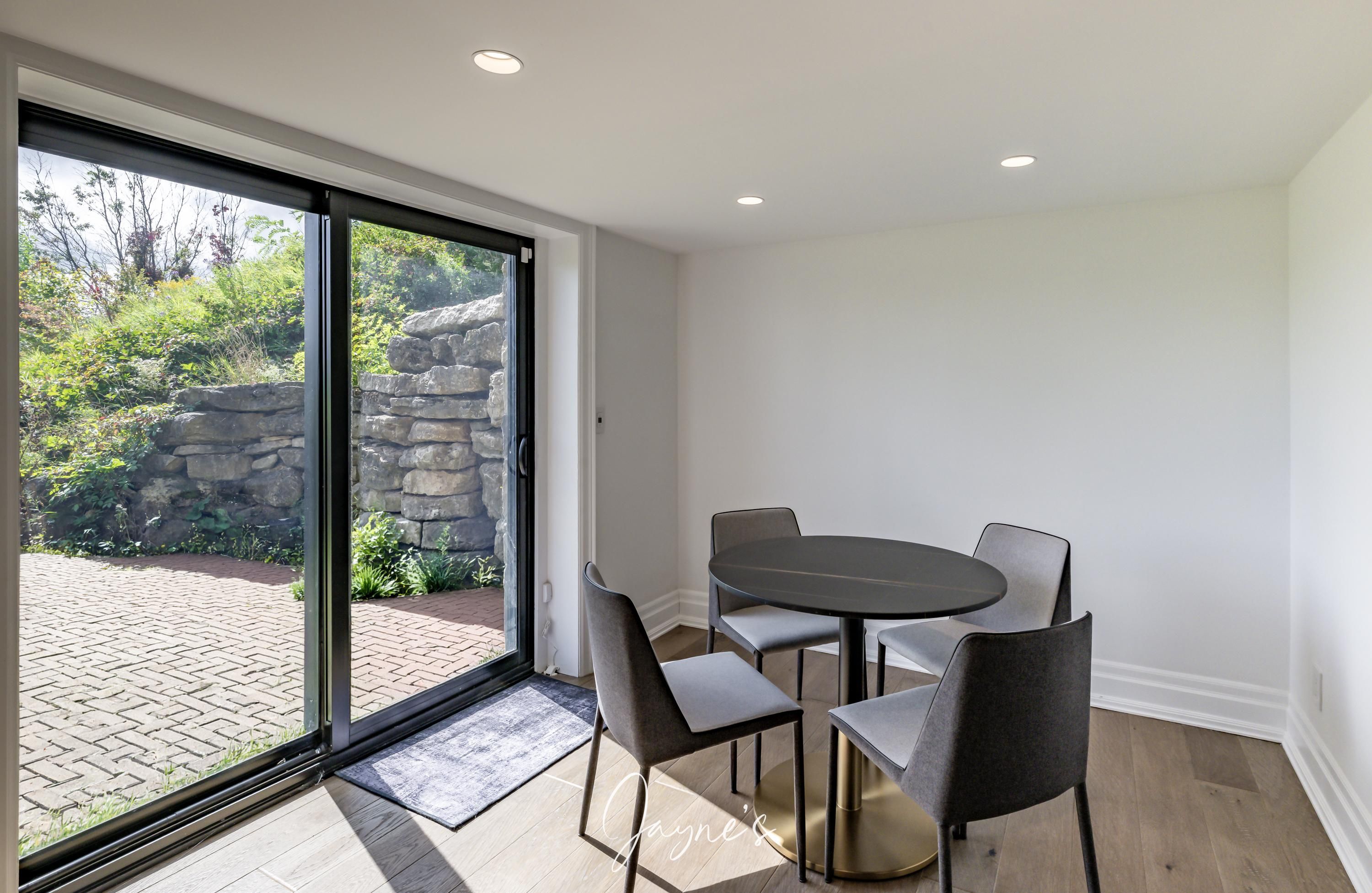 Una habitación moderna con un cerramiento de vidrio corredero que da a un patio, una mesa redonda con cuatro sillas y una pequeña alfombra en el suelo.