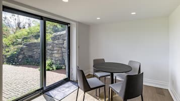 Una habitación moderna con un cerramiento de vidrio corredero que da a un patio, una mesa redonda con cuatro sillas y una pequeña alfombra en el suelo.