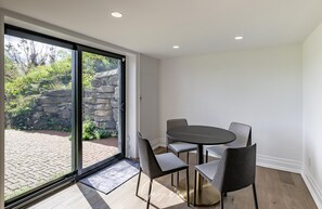 Quarto moderno com porta de vidro deslizante para um pátio, uma mesa redonda com quatro cadeiras e um tapete pequeno no chão.